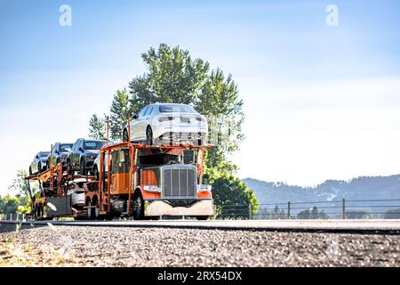 Leuchtend orangefarbener Industriestandard-Autotransporter, klassischer Träger, großer Auflieger, Sattelzugmaschine für den Transport von Autos, zweistufiger hydraulischer, modularer Auflieger, dri Stockfoto