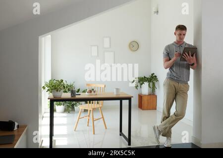 Junger Mann, der sich an die Wand lehnt, wenn er den Vertrag auf einem Tablet-Computer liest Stockfoto