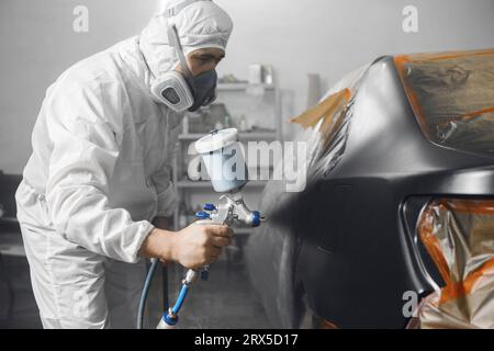 Karosseriefarbenlackierer mit Luftpistolen-Spritzfarbe auf Fahrzeugteil im Lackierraum des Kfz-Wartungsdienstes. Stockfoto