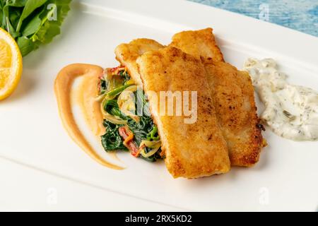 Gebratenes Panga-Filet mit Gemüse und Zwiebeln an der Seite und Spinat darunter Stockfoto