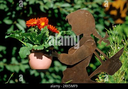Mädchenfigur mit roter Gerbera, Gartenfigur mit Blumentopf, Mädchenplastik mit roter Gerbera-Figur mit Blumentopf Stockfoto