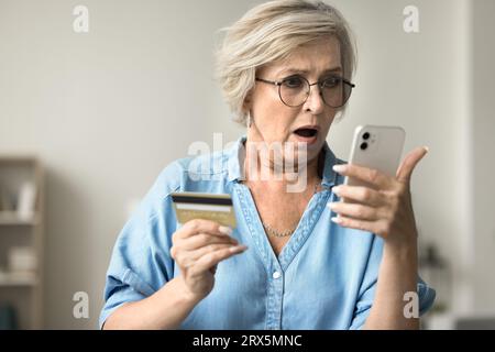 Schockierte, besorgte, reife Frau in Brille, die Kreditkarte hält Stockfoto