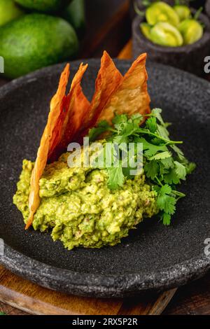 Avocado-Dip-Guacamole mit knusprigen Tortillas auf schwarzem Steinteller auf Holztisch Stockfoto