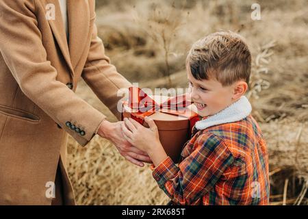 Mutter schenkt dem glücklichen Sohn im Feld eine Geschenkbox Stockfoto