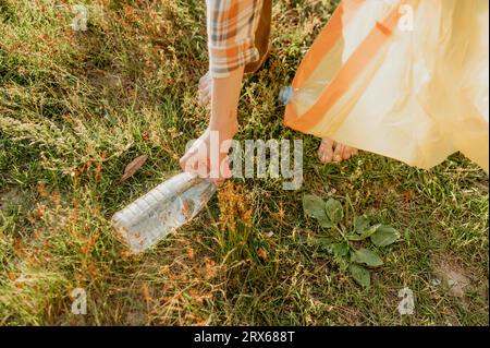 Hand des Jungen, der Plastikflasche auf Gras aufnimmt Stockfoto