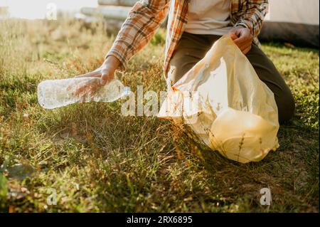 Junge, der Plastikflasche sammelt, kniend auf Gras Stockfoto