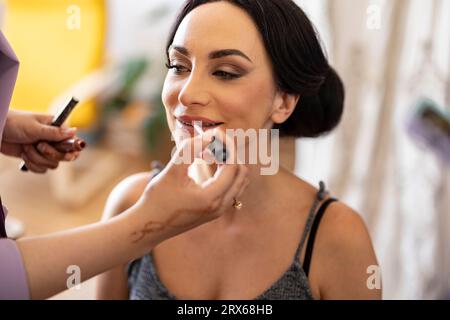 Hand des Make-up-Künstlers, der Lippenstift auf die Lippen der Braut aufträgt Stockfoto