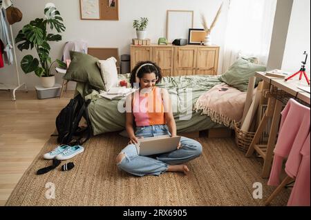 Glückliches Mädchen, das zu Hause kabellose Kopfhörer mit Laptop trägt Stockfoto