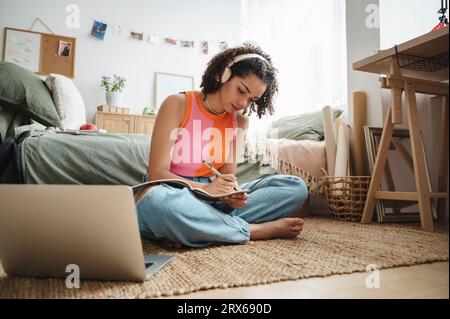 Teenager-Mädchen, das Hausaufgaben macht und zu Hause auf dem Teppich sitzt Stockfoto