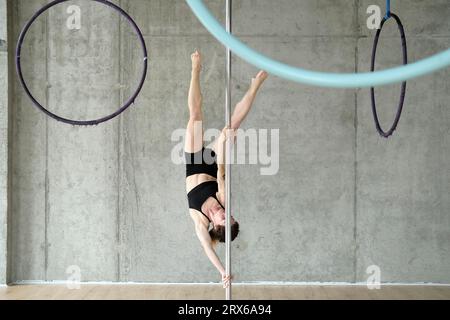 Frau, die Gymnastik an der Stange vor der Betonwand übt Stockfoto