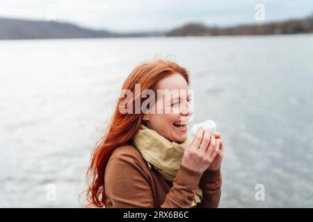 Rothaarige Frau, die Taschentuch hält und am See lacht Stockfoto