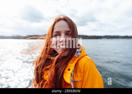 Lächelnde Rothaarige mit langen Haaren vor dem See Stockfoto