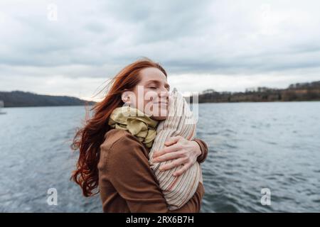 Lächelnde Frau umarmt Kissen am See Stockfoto