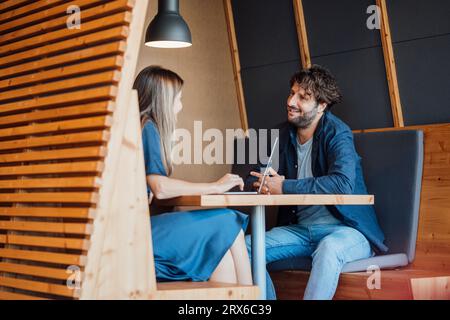 Lächelnde Geschäftsleute sitzen mit Laptop und reden im Büroschrank Stockfoto