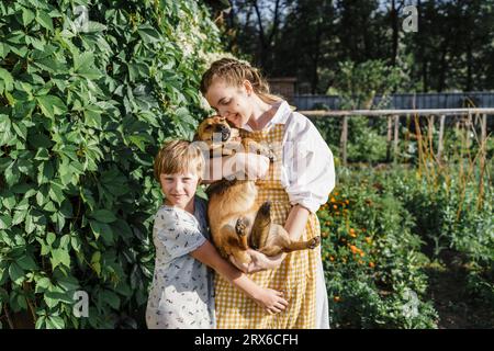 Mutter und Sohn umarmen den Hund an sonnigen Tagen im Hinterhof Stockfoto