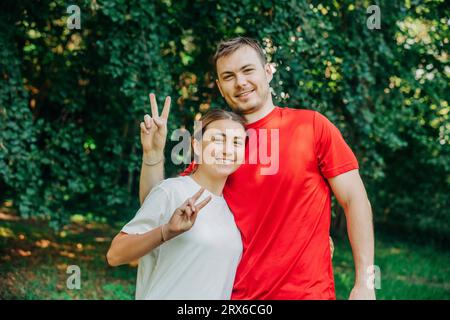 Lächelnder Bruder und Schwester zeigen Friedenszeichen im Park Stockfoto