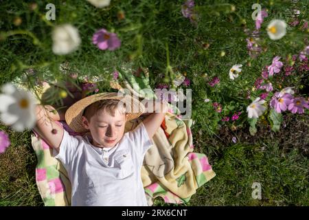 Lächelnder Junge mit Hut, der auf einer Decke im Garten liegt Stockfoto