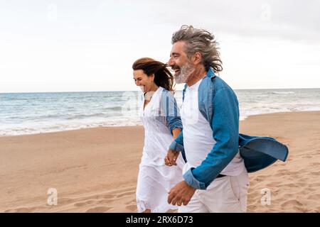 Glückliches Seniorenpaar, das gerne auf dem Meer auf dem Sand spazieren geht Stockfoto