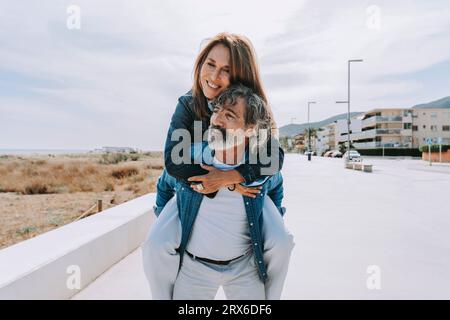 Älterer Mann, der eine Frau mit Schweinehund begleitet und am Wochenende zum Strand läuft Stockfoto