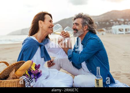 Glückliches Seniorenpaar, das am Strand Wein durch eine Weinbrille trinkt Stockfoto