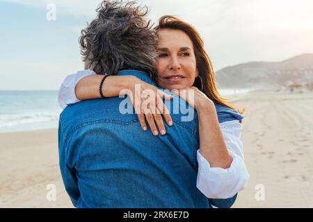 Glückliche ältere Frau umarmt Mann am Strand Stockfoto