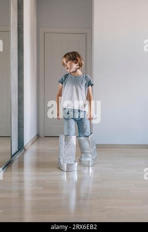 Junge, der handgefertigte Astronautenstiefel trägt und zu Hause zu Fuß geht Stockfoto