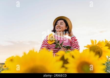 Lächelnde reife Frau mit Hut in Sonnenblume abgelegt Stockfoto