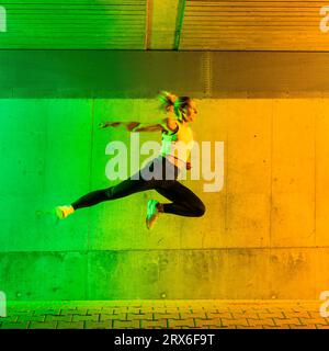 Frau, die Sportkleidung trägt, springt in der Nähe einer neonfarbenen Wand Stockfoto