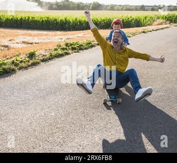 Glücklicher Mann, der Skateboarding genießt und Enkel, der ihn von hinten schiebt Stockfoto