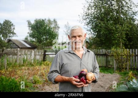 Lächelnder Mann, der Zwiebeln im Garten hält Stockfoto