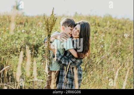 Mutter, die einen Strauß Blumen hält und den Sohn auf dem Feld umarmt Stockfoto