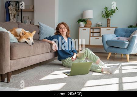 Junge Frau, die Waliser Corgi-Hund auf dem Sofa im Wohnzimmer ansieht Stockfoto