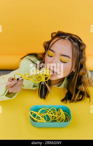 Junge Frau, die Wired Nudeln am Tisch im Studio isst Stockfoto