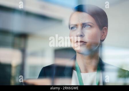 Durchdachte Geschäftsfrau im Büro durch Glas gesehen Stockfoto