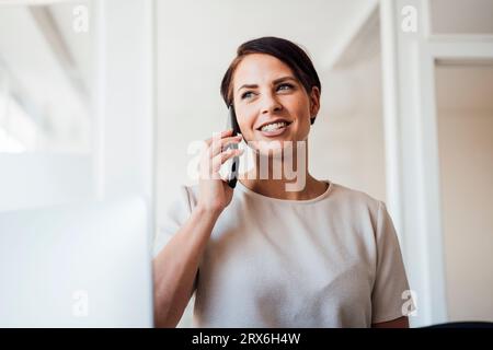 Lächelnde Geschäftsfrau, die am Arbeitsplatz auf dem Handy spricht Stockfoto