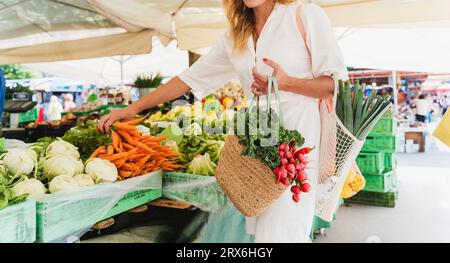 Frau, die Karotten auf dem Bauernmarkt kauft Stockfoto