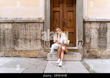 Lächelnde Frau, die mit einem Haufen Sonnenblumen vor der Holztür sitzt Stockfoto