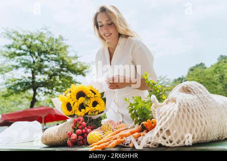 Glückliche Frau mit einem Haufen Sonnenblumen und Lebensmitteln am Tisch auf dem Markt Stockfoto