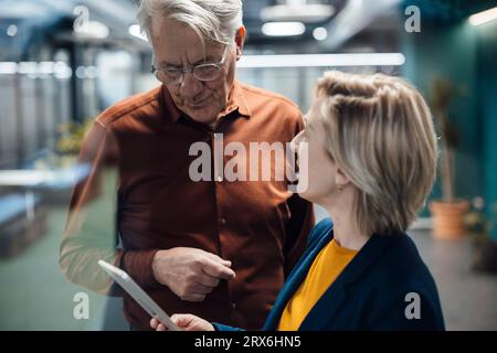 Geschäftsfrau, die einen Tablet-PC hält und mit Kollegen am Arbeitsplatz diskutiert Stockfoto