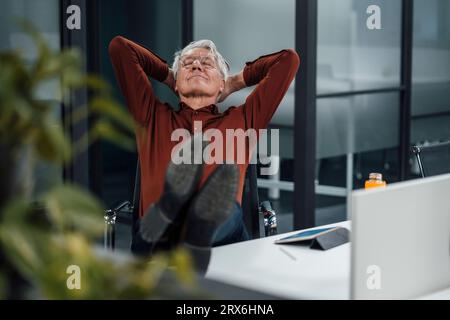 Leitender Geschäftsmann mit Händen hinter dem Kopf, der sich am Schreibtisch im Büro entspannt Stockfoto