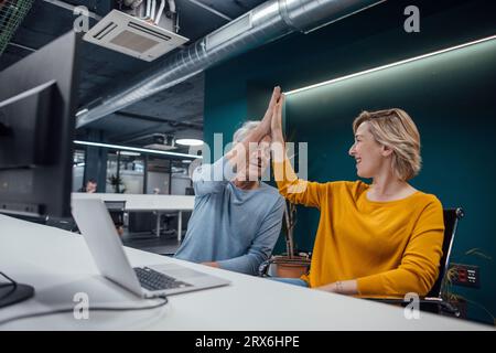 Geschäftskollegen, die sich am Schreibtisch im Büro gegenseitig High-Five geben Stockfoto