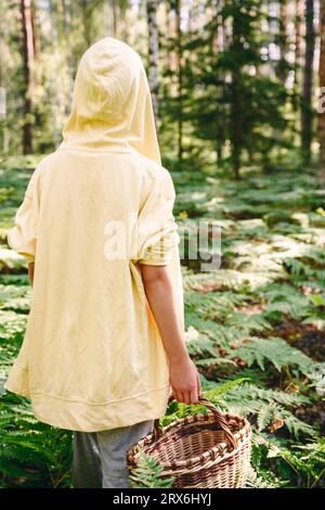 Junge in gelbem Hoodie mit Korb, der im Wald spaziert Stockfoto