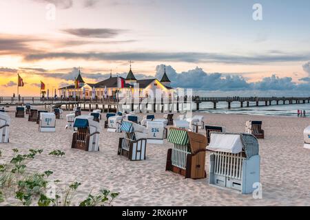 Deutschland, Mecklenburg-Vorpommern, Ahlbeck, Strandliegen mit Kapuze bei Sonnenuntergang mit Pier und Badehaus im Hintergrund Stockfoto