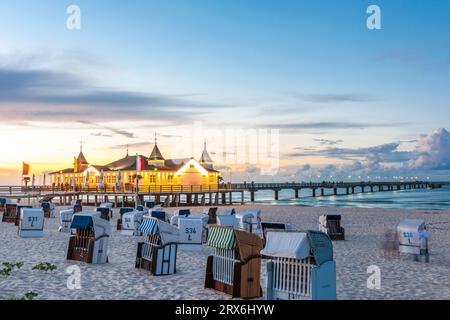 Deutschland, Mecklenburg-Vorpommern, Ahlbeck, Strandliegen mit Kapuze bei Sonnenuntergang mit Pier und Badehaus im Hintergrund Stockfoto