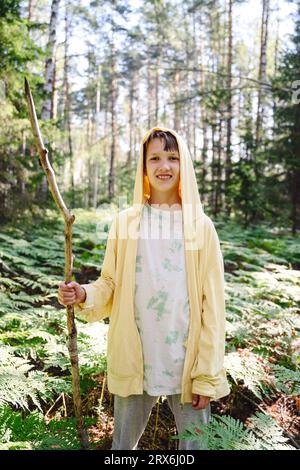 Lächelnder Junge mit Stock, der im Wald steht Stockfoto