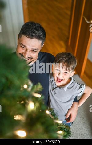 Lächelnder Vater und Sohn mit Blick auf den geschmückten Weihnachtsbaum Stockfoto