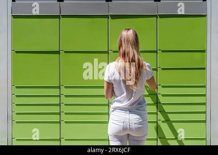 Junge Frau, die an sonnigen Tagen automatisierte Paketschränke benutzt Stockfoto