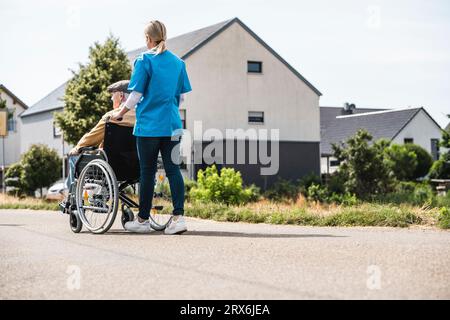 Gesundheitsfachkraft, die im Rollstuhl sitzenden älteren Mann schiebt Stockfoto