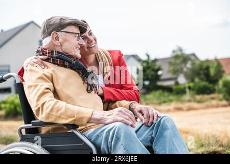 Lächelnde Frau, die einen älteren Mann umarmt, der im Rollstuhl sitzt Stockfoto