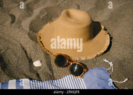 Sonnenhut neben Sonnenbrille auf Sand am Strand Stockfoto